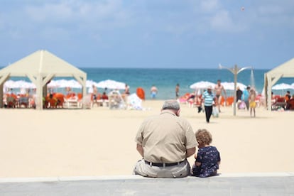 Un abuelo se sienta con su nieta en el poyete de un paseo marítimo.