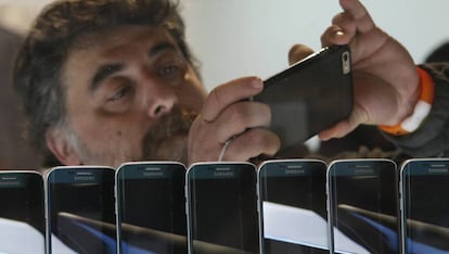 Un hombre inspecciona un teléfono móvil en una exposición. 