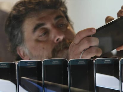 Un hombre inspecciona un teléfono móvil en una exposición. 