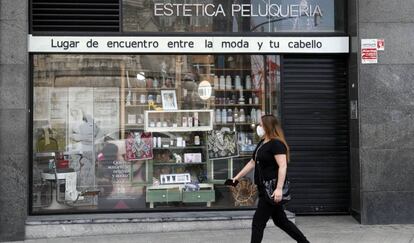 Una mujer con mascarilla pasa frente a una peluquería cerrada en Bilbao.