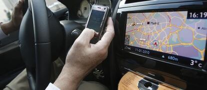 Un conductor mira su teléfono móvil, utiliza el GPS y pone un CD en su vehículo.