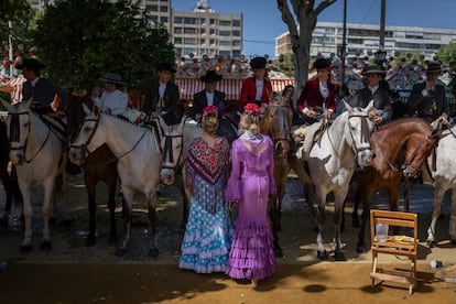 Dos chicas vestidas de flamenca hablan con un grupo de jinetes en una parada, este lunes.