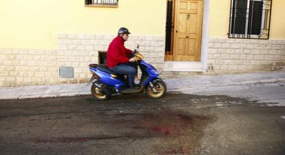 Un hombre pasa con su ciclomotor junto a los restos de sangre de la mujer degollada anoche en Benaguasil.