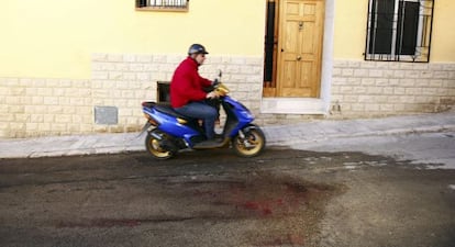 Un hombre pasa con su ciclomotor junto a los restos de sangre de la mujer degollada anoche en Benaguasil.