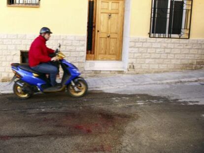 Un hombre pasa con su ciclomotor junto a los restos de sangre de la mujer degollada anoche en Benaguasil.