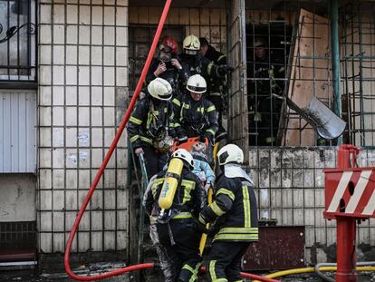 Los bomberos trasladan el cuerpo de una mujer muerta por los bombardeos en un edificio de Kiev, el martes.