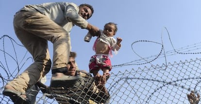Un hombre levanta a un niño sirio por encima de la alambrada de espinos en la frontera con Turquía.