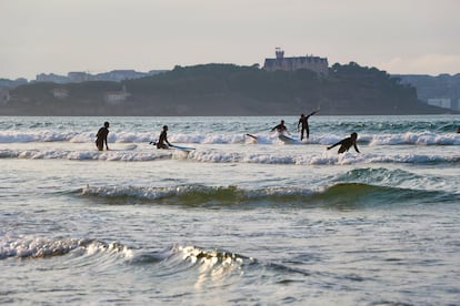 Surfistas cogiendo olas en Somo. Al fondo, el palacio de la Magdalena, en Santander (Cantabria).