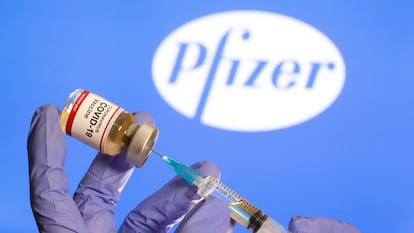 Uma mulher segura um pequeno frasco com o rótulo "Vacina COVID-19" e uma seringa médica na frente do logotipo da Pfizer.