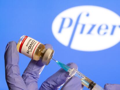 Uma mulher segura um pequeno frasco com o rótulo "Vacina COVID-19" e uma seringa médica na frente do logotipo da Pfizer.