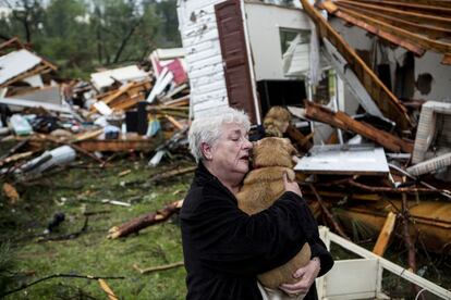 Uma mulher abraça sua cachorra após resgatá-la com vida depois que o tornado destruiu sua casa.