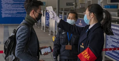 Personal de seguridad toma la temperatura de un viajero en la estación de tren de Nanning.