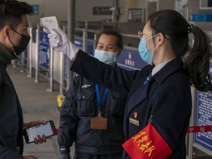 Personal de seguridad toma la temperatura de un viajero en la estación de tren de Nanning. 