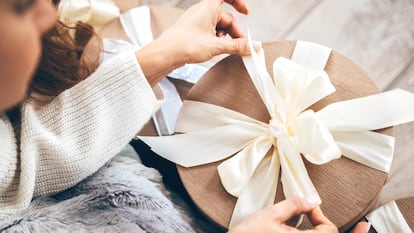 Plano detalle de una mujer abriendo un regalo con un gran lazo.