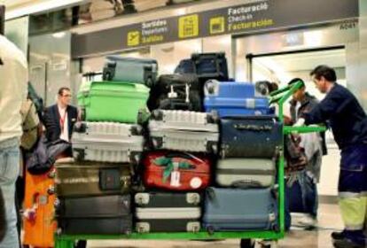 Dos operarios trasladan un carro con varias maletas a la espera de la salida del vuelo en el aeropuerto de El Prat de Barcelona. EFE/Archivo