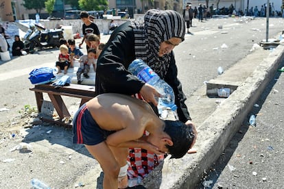 Una mujer ayuda a un niño a lavarse la cabeza en una calle mientras los residentes de Beirut permanecen en las calles después de huir de sus hogares tras los ataques israelíes.