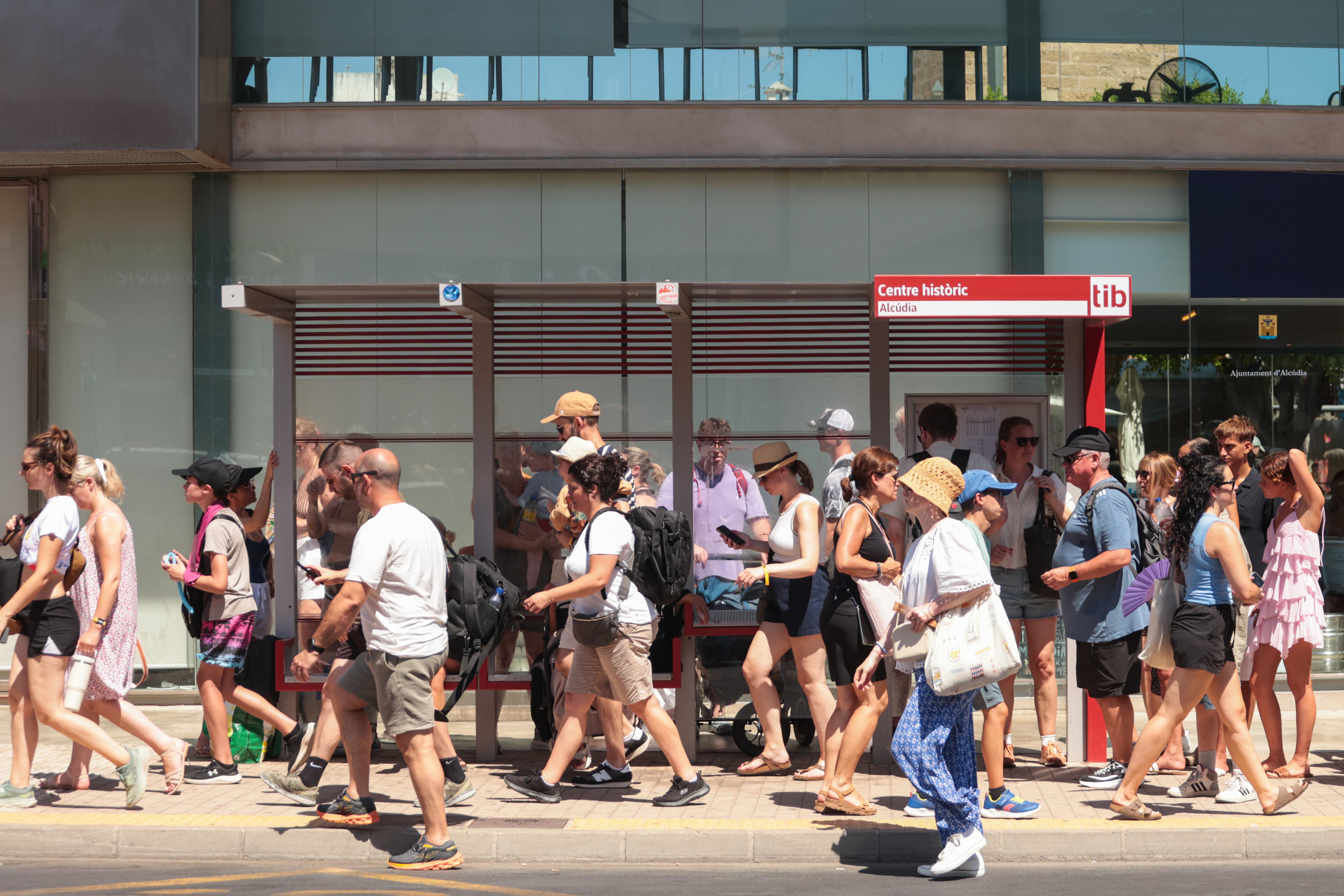 Turistas en una parada de buses en Alcudia, este domingo.