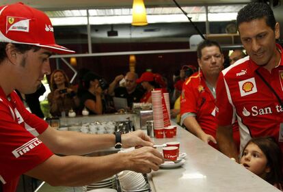 El piloto asturiano ha dejado por unos minutos su bólido y se ha puesto tras la barra para servir cafés a los seguidores de Ferrari.