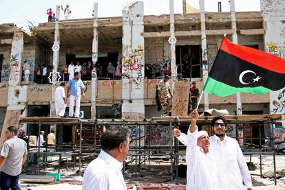 Un hombre ondea la bandera de la rebelión mientras numerosos tripolitanos visitan el fortín de Gadafi en Bab el Azizia.