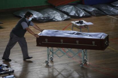 Un hombre empuja un féretro ante una fila de cadáveres, en un gimnasio de Concepción.