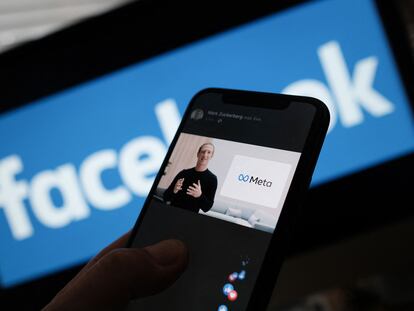 Una persona observa en su móvil cómo el fundador de  Facebook, Mark Zuckerberg, presenta el logo de Meta.