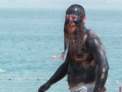 Un judío ultraortodoxo pasea por una playa del mar Muerto totalmente cubierto de barro.