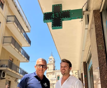 De izquierda a derecha, Elio Morale y Biagio Cantone, debajo del termómetro de su farmacia en Floridia, Sicilia, el municipio donde en 2021 se registró el récord europeo de calor, 48,8 grados (medido en una estación meteorológica).