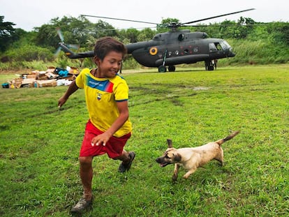 Luis Napa y su perro &quot;Pelusa&quot; juegan en el estadio de Pedernales, Ecuador, mientras un helic&oacute;ptero del Ej&eacute;rcito deja ayuda humanitaria.