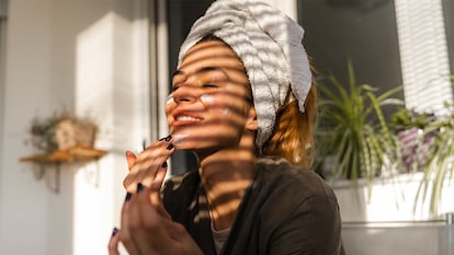 Una chica con una toalla en la cabeza echándose crema en la cara.