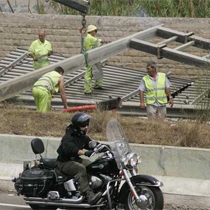 Unos operarios retiran la estructura del panel derribado por el camión en la V-30 de Valencia