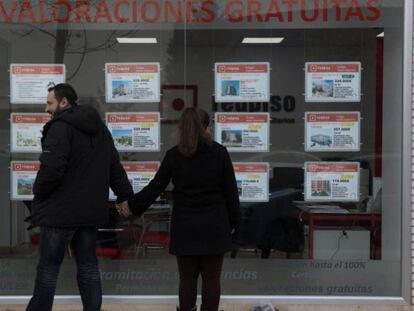 Dos jóvenes miran un escaparate con anuncios de pisos en el Ensanche de Vallecas (Madrid). 