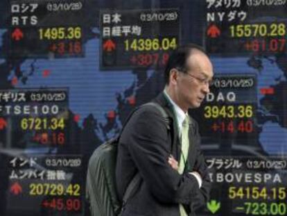 Un peatón camina junto a una pantalla informativa que muestra información bursátil en Tokio (Japón). EFE/Archivo