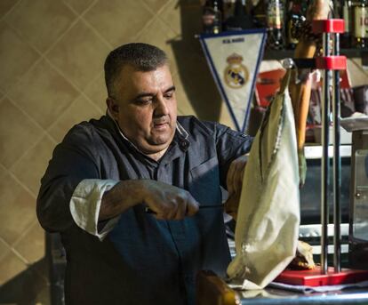 Gregorio Pifarré, encarregat del Casal d'Alfés, l'únic restaurant el poble, tallant pernil. Al fons, la banderola del Reial Madrid.