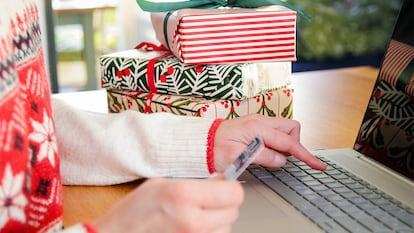Una persona comprando con regalos en la mesa a través del ordenador.