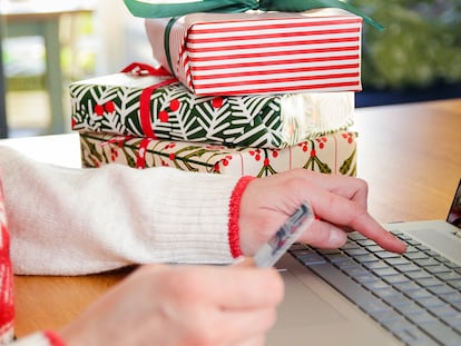 Una persona comprando con regalos en la mesa a través del ordenador.
