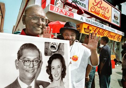 Ben Ali posa en esta imagen de 2003 con Joe Johnson, un habitual del Ben's Chili Bowl, sosteniendo la misma imagen con su esposa Virginia de 1958, el mismo año que abrió el local en la U Street. Johnson ha comido en el local desde que era un niño. Cada año un grupo de vecinos se reúnen en el 22 de agosto en los alrededores del restaurante para celebrar su aniversario.