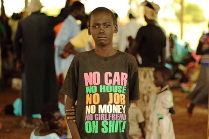 Un niño refugiado con polio espera registrarse para obtener un nuevo hogar en Nyumanzi. Viste una camiseta dónde se lee en inglés: “Sin coche, sin casa, sin trabajo, sin dinero, sin novia, Oh mierda!”