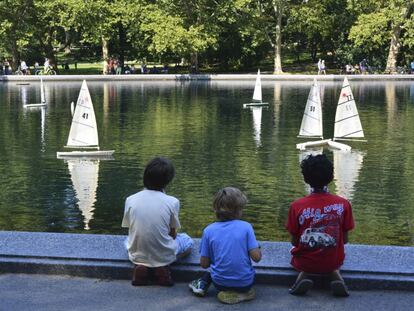Tres niños juegan con sus barcos de vela en un estanque.
