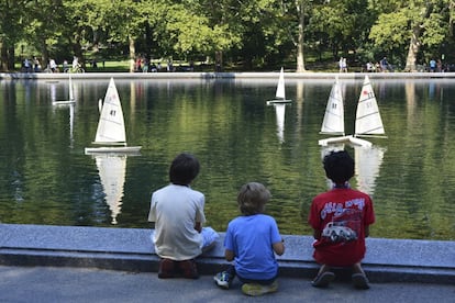 Tres niños juegan con sus barcos de vela en un estanque.