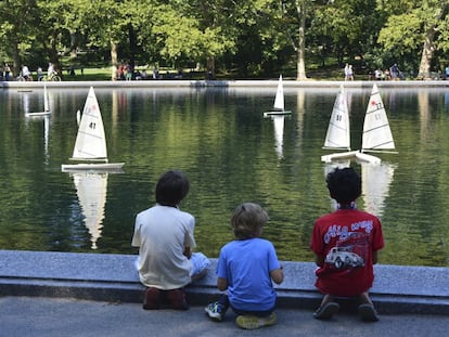 Tres niños juegan con sus barcos de vela en un estanque.