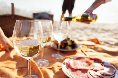 Una imagen de placer estival: sirviendo un vino espumoso, en pleno pícnic playero.