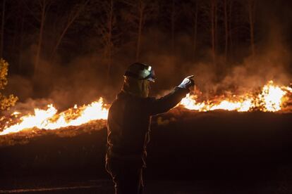 Las llamas alcanzan la carretera en el municipio de Ribas do Sil. Un bombero realiza indicaciones a sus compañeros para las labores de extinción del fuego