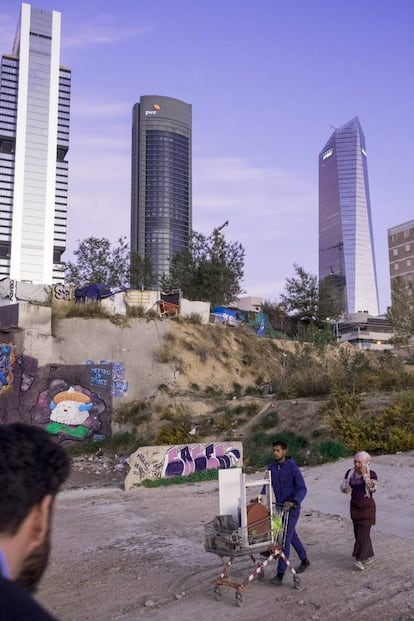 Una pareja que vive en las chabolas camina por una zona de 'parking' con un carro de chatarra, frente a las Cuatro Torres del paseo de la Castellana. Son los más pobres de los pobres y ni siquiera figuran en el mapa de la renta del INE.