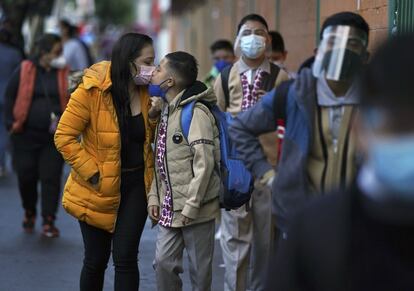 Un estudiante recibe un beso de despedida de su madre antes de entrar a la escuela.