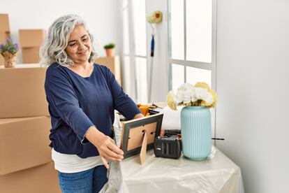 Mujer de mediana edad sonriendo feliz sosteniendo una foto en su nuevo hogar.