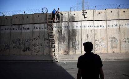 Un hombre observa cómo dos jóvenes palestinos intentan cruzar el muro de separación usando una escalera al lado del puesto de control militar israelí de Qalandia, en Cisjordania.