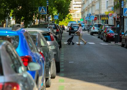Una mujer cruza una calle en Madrid con vehículos aparcados en la zona de estacionamiento regulado.