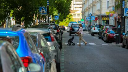 Una mujer cruza una calle en Madrid con vehículos aparcados en la zona de estacionamiento regulado.
