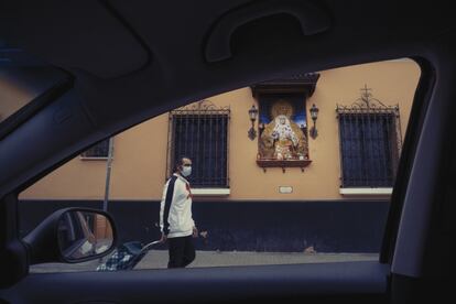Un hombre, con mascarilla y carro de la compra, pasa por delante de una imagen de la Virgen Macarena, en la casa museo de la Hermandad, el 20 de abril.