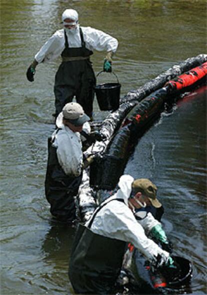 Tres operarios recogen fuel en medio del río Fluvià.